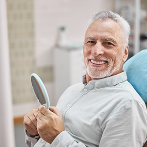 Senior man smiling while holding emergency dentist's mirror