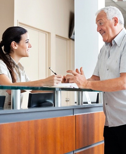A female dental receptionist talking to a male patient about the cost of his dental implant treatment