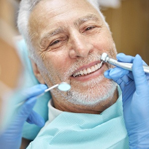 An older man smiles while a dentist examines his dental implants during a follow-up exam