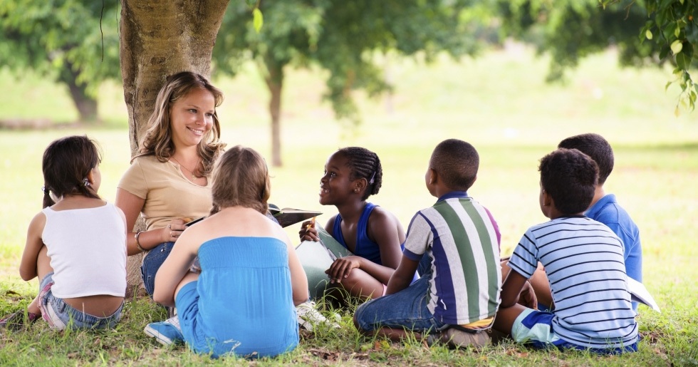 Woman reading to a group of children under a tree