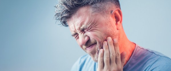 Man in need of restorative dentistry holding cheek in pain