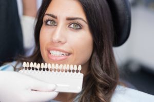 dentist holding a row of veneers in front of a patient’s smile 